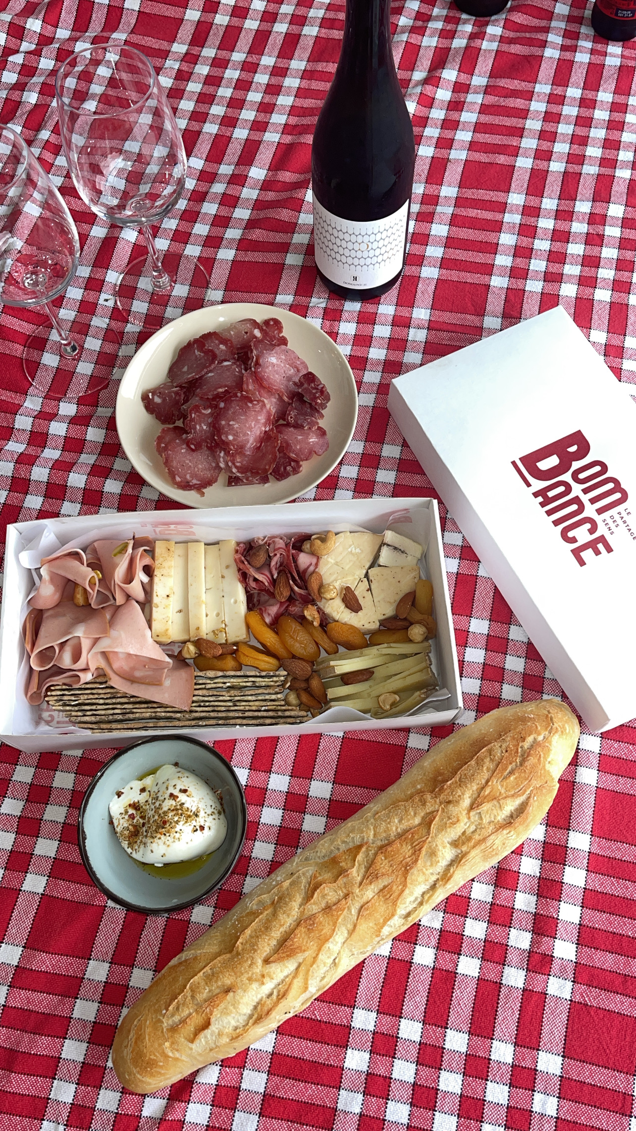 Box apéro avec du pain, du vin et une nappe à carreau rouge